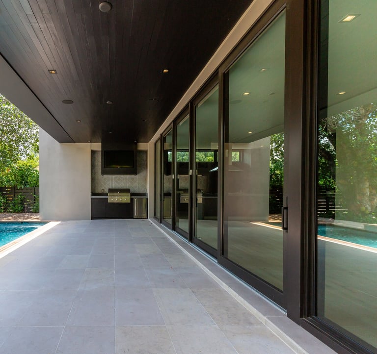 the outside patio of a luxury home with an outdoor grill, pool and deck with sliding glass doors