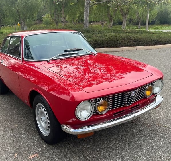 A photo of a red 1974 Alfa Romeo GTV 2000 in a park setting.