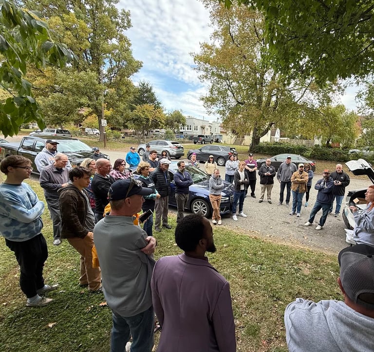a group of people standing around a table with a car in the background