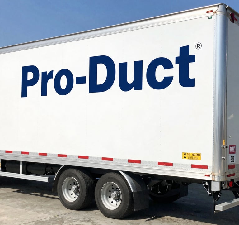 A low-angle architectural photograph of the Pro-Duct manufacturing plant in Riyadh. The modern facade features dark charcoal blue steel panels and bright industrial windows against a clear twilight sky.