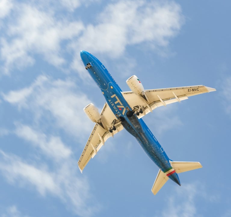 An ITA Airways airplane flying overhead against a clear sky
