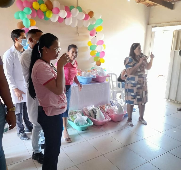 A woman speaking at a community event with health kits and colorful balloon decorations.