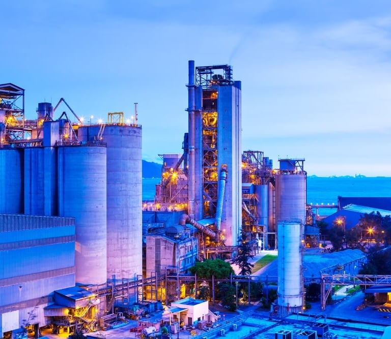 Industrial manufacturing plant with large storage silos and towers illuminated at twilight.