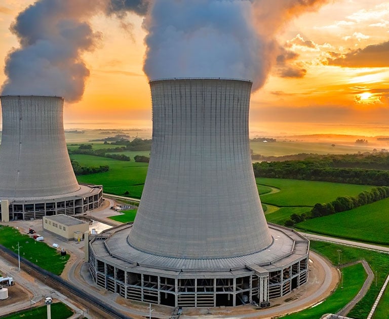 Aerial view of a nuclear power plant with two cooling towers emitting steam during a vibrant sunset.