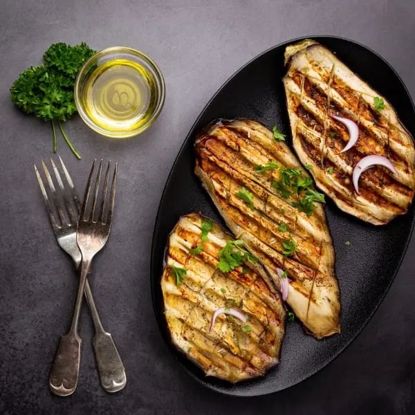 Aubergines grillées sur assiette noire avec bol d'huile d'olive