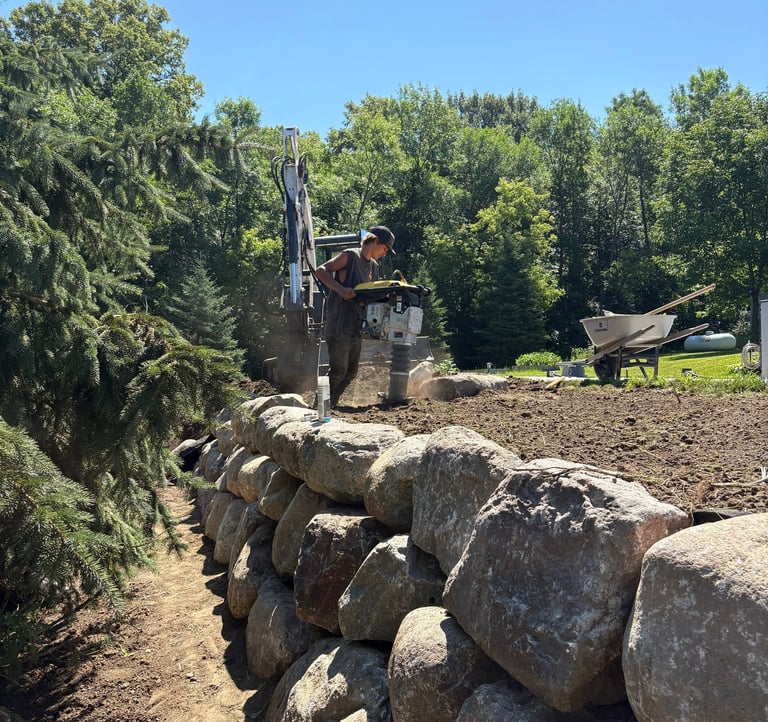 Arcadia Landscapes employee compacting dirt around boulder wall