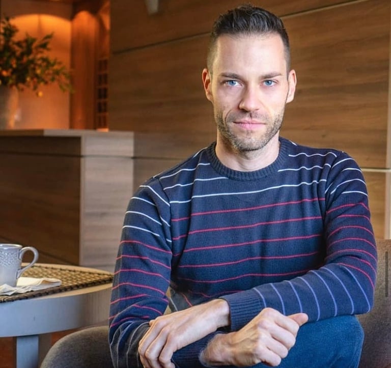 Uma foto do proprietário da empresa: homem jovem, com barba, olhos azuis, vestindo malha azul.