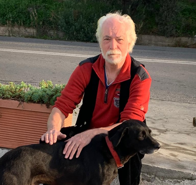 Mann in der Hocke an einer Straße streichelt einen schwarzen Hund. Er ist freischaffender Künstler.