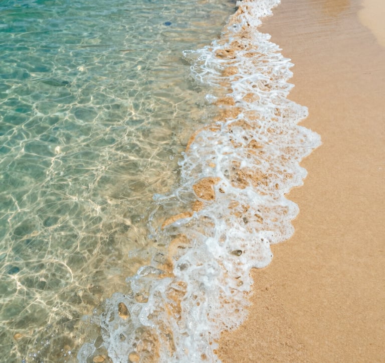 Close-up shot of crystal clear turquoise waves gently washing over golden sand in Puerto Escondido. High-end photography with soft lighting and a focus on the natural beauty of a Mexican coastal paradise.