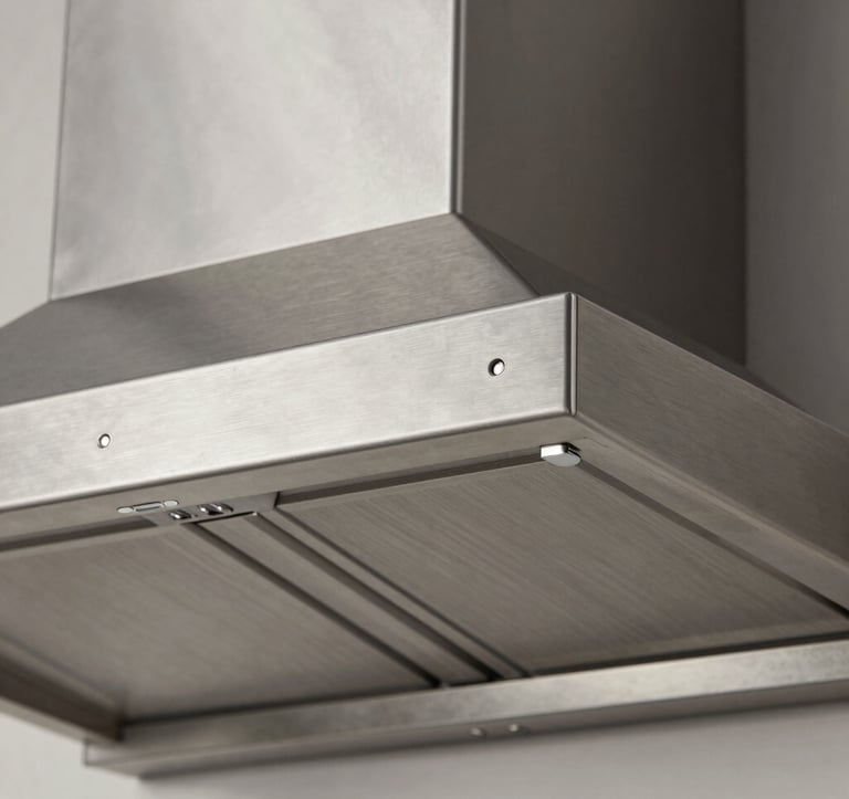 Detailed architectural close-up of the precision-engineered stainless steel surface of a range hood. The texture is brushed inox, showing clean lines and sophisticated metallic reflections under soft studio lighting.