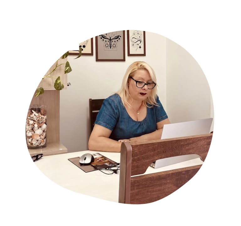 A blonde woman wearing glasses works on her laptop at a home office desk with modern decor.