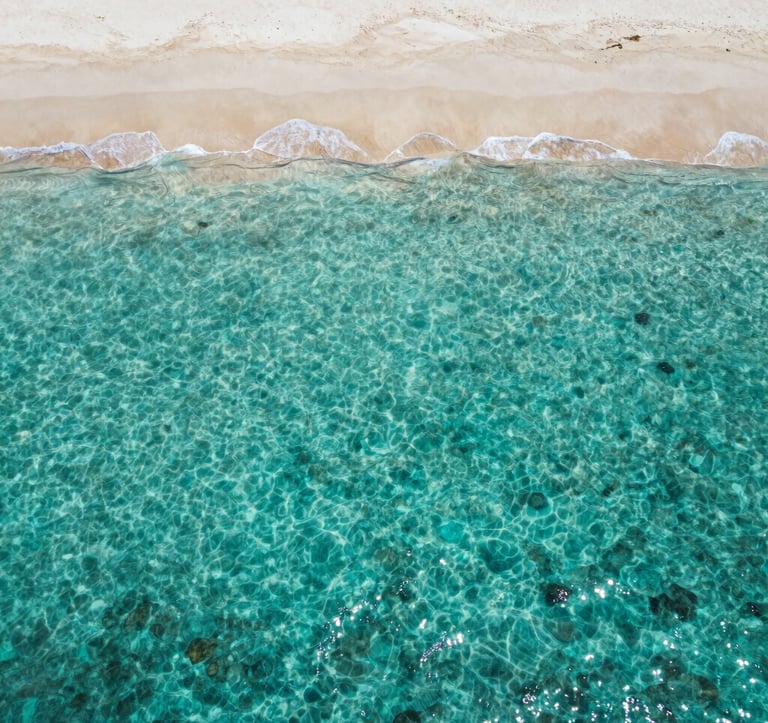 An aerial top-down photograph of a remote, crystalline turquoise lagoon in the Indian Ocean, with a thin strip of ivory sand. The composition is minimalist and spacious, capturing the essence of private access and solitude for the Global / Discerning English-speaking elite.