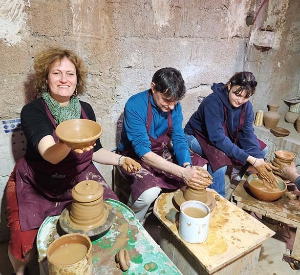 Une femme est assise devant un tour de poterie en train de montre une coupe en argile