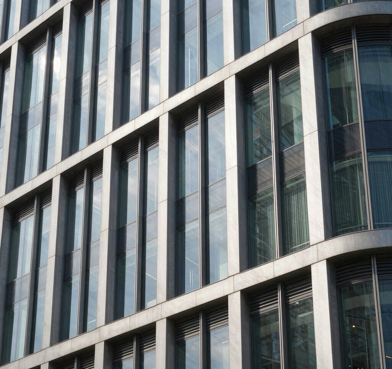 A close-up photograph of a modern building facade featuring premium glass and steel textures. The composition is sharp and architectural, showcasing sophisticated construction quality under bright daylight in a South Asian city.