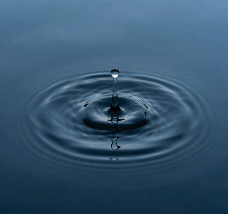 A minimalist macro photograph of a single ripple in a dark, steel blue pool of water. The composition is centered and calm, emphasizing perfect symmetry and the beauty of a single movement in a quiet landscape.