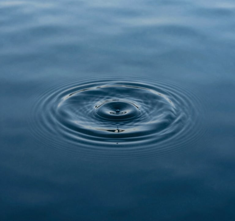 A minimalist photograph of a single ripple expanding on the surface of a deep steel blue pool of water. The composition is tight and focused, emphasizing the profound stillness of the surrounding liquid. Soft, diffuse lighting.