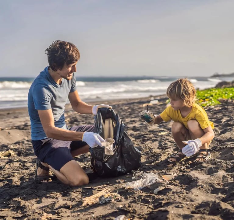 A father and his son sitting on the beach, collecting garbage into a black plastic bag