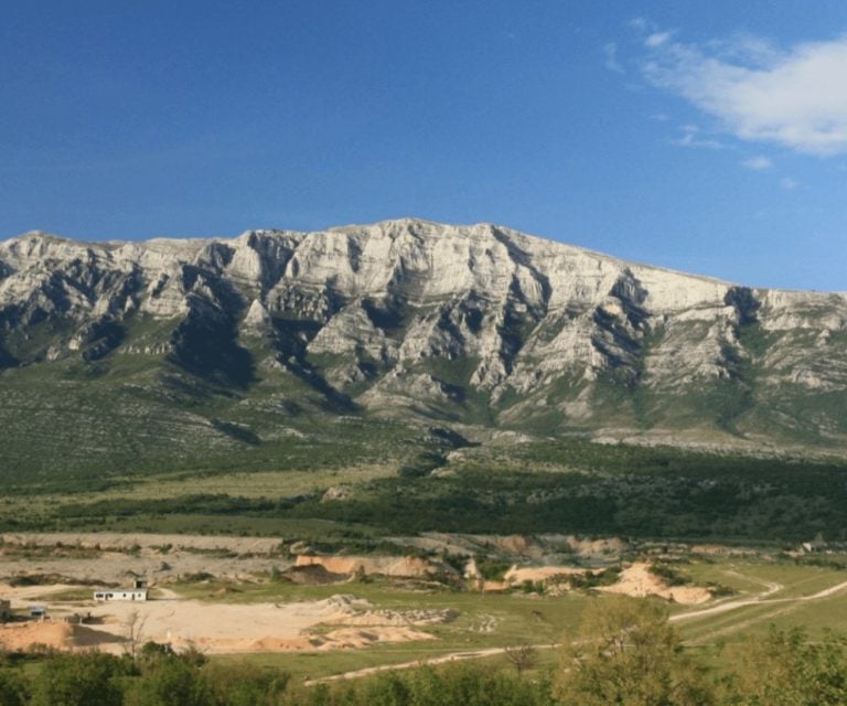Panoramic view of Dinara mountain, showcasing rugged peaks and lush green valleys under a clear blue
