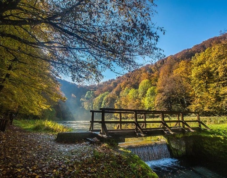 Waterfall cascading through lush forest and below wooden bridge in Papuk UNESCO Geopark.