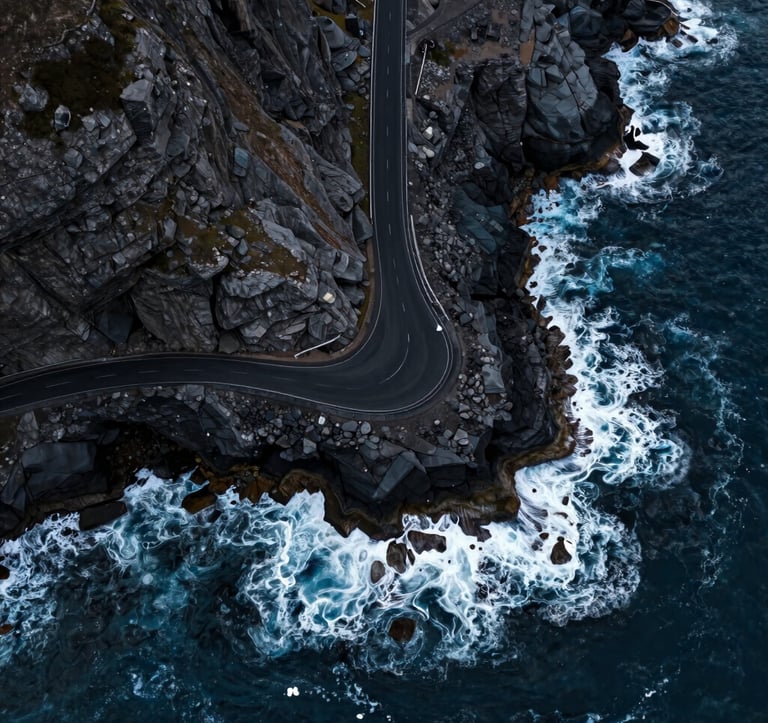 A high-altitude drone shot looking straight down at a rugged coastline with a single road hugging the cliffs. The deep blue water contrasts with the Midnight Black asphalt. Soft Pearl foam from the waves creates a dynamic pattern. Cinematic aerial photography in a Global / International location.