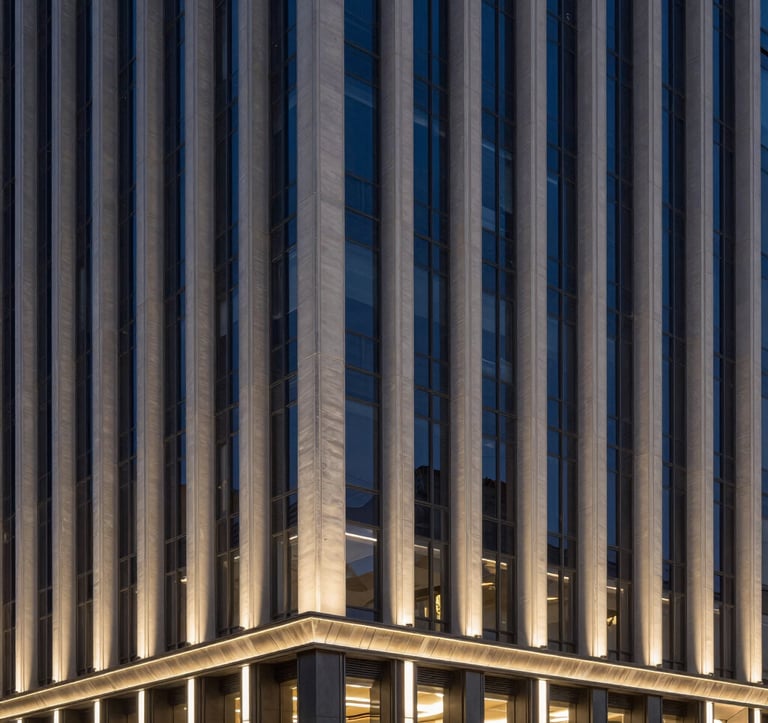 The sleek architectural facade of a luxury contemporary building in Seoul at night. The structure features clean vertical lines and is illuminated by a subtle deep navy and soft gold lighting scheme. The composition is clean and modern, evoking high-end urban elegance.