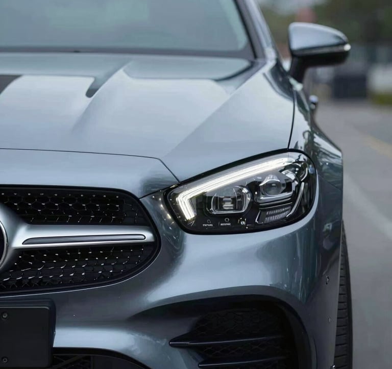 A close-up shot of the front grille and headlight of a luxury European car. The design is sharp and aggressive. The lighting is cold and professional, utilizing #B8CEDE for the metallic glints and #0A1128 for the deep recesses.