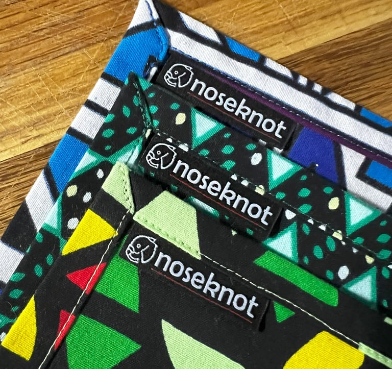Three vibrant Noseknot handkerchiefs showing the stitching, corners and Noseknot labels