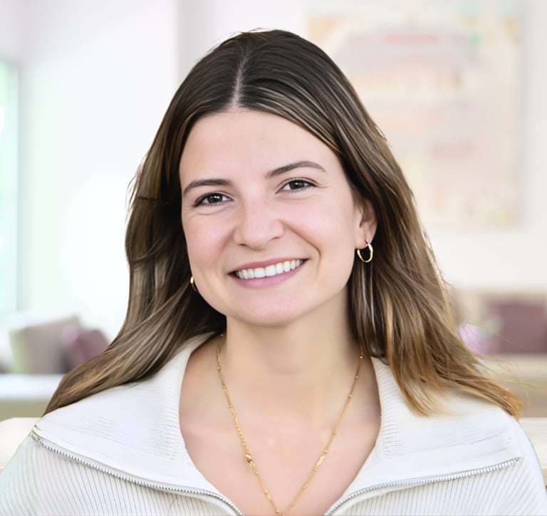 A smiling professional woman with brown hair wearing a white zip-up sweater and gold jewelry.