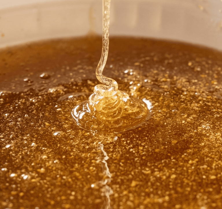 Golden raw honey pouring into a container, showing thick texture and air bubbles.