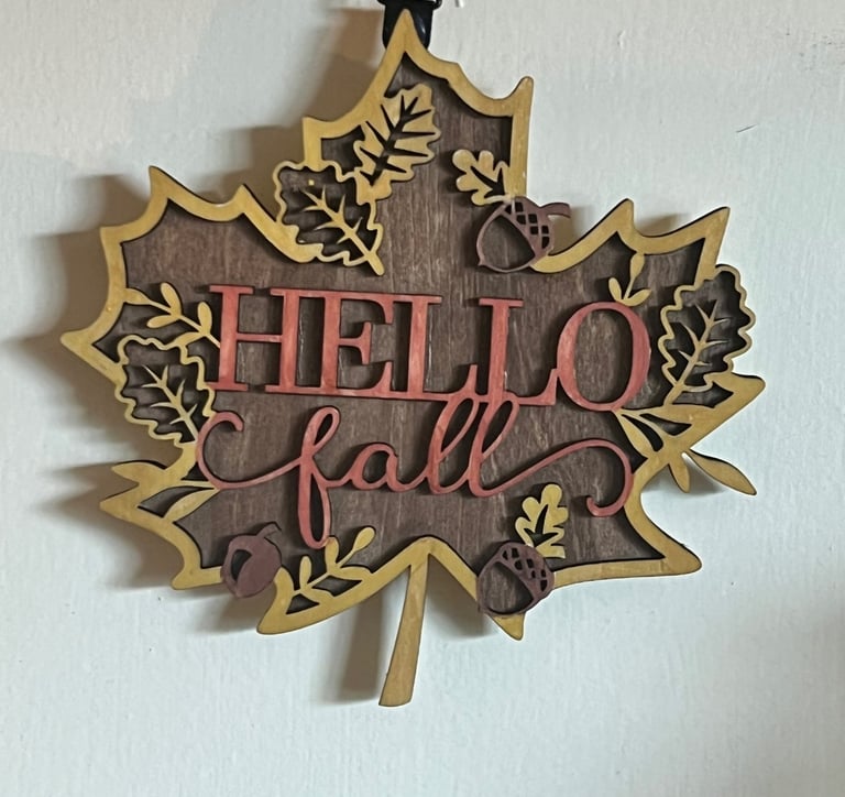 Leaf-shaped wooden wall sign saying "Hello Fall" with acorn and leaf accents.