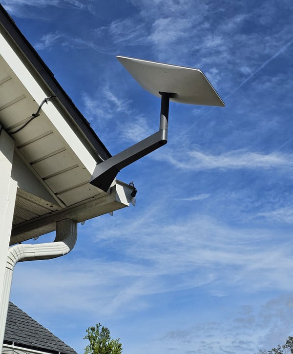 A Gen3 Starlink satellite internet dish mounted on a residential roof eave against a blue sky.