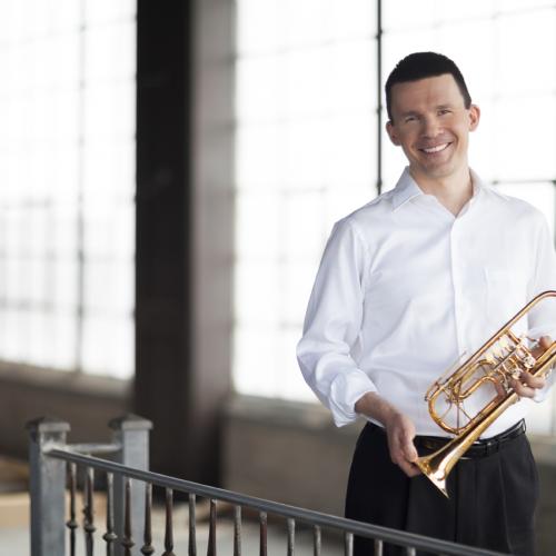 Man wearing white button down shirt, holding a trumpet and smiling.