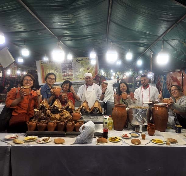 a group of people standing around a table with food