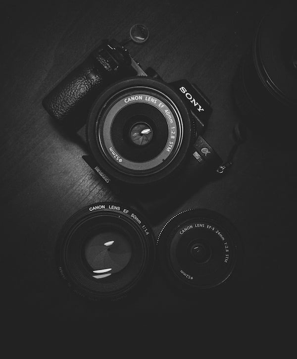 A black and white photo of a Sony digital camera with 3 Canon lenses.