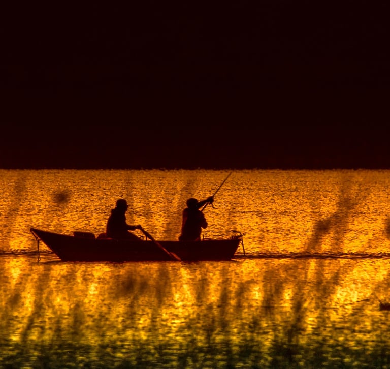 two people fishing in a lake at sunset
