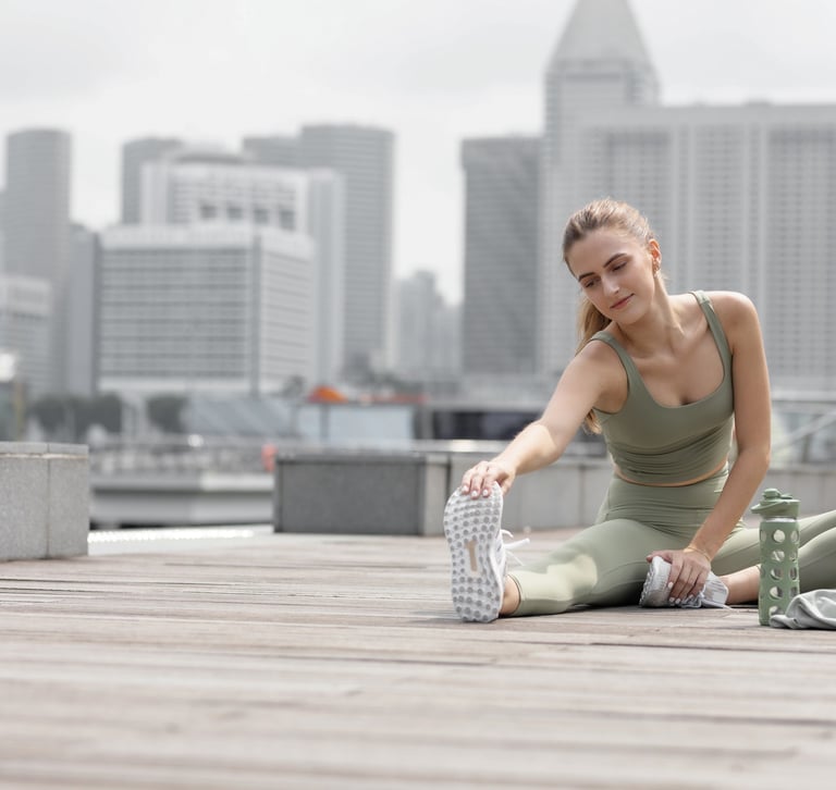 A woman wearing athletic wear, sitting outside with an urban background, stretching before exercising.