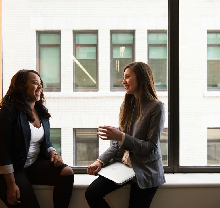Two diverse female professionals discussing business strategy during a meeting by an office window.