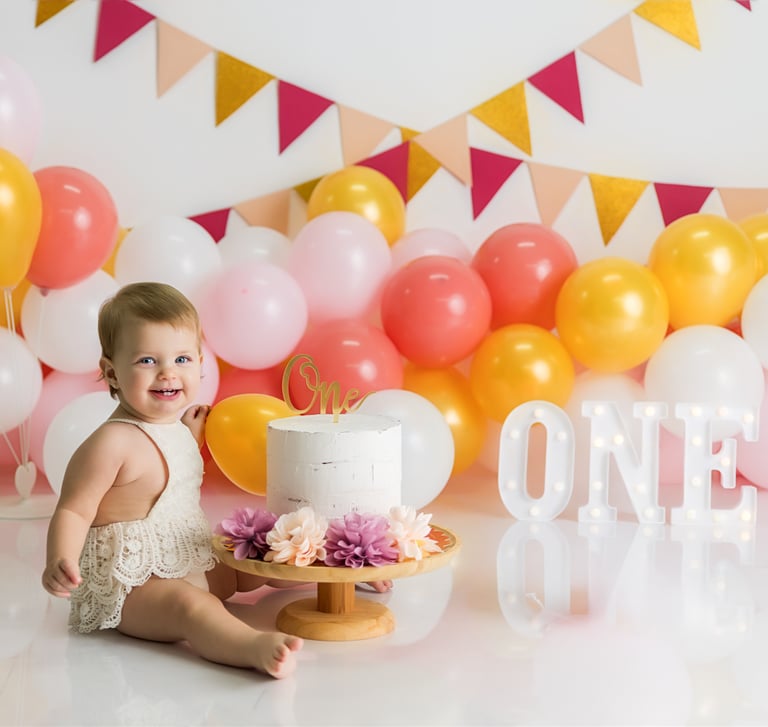 bebé sentada junto a tarta delante de globos en la sesión de smash cake