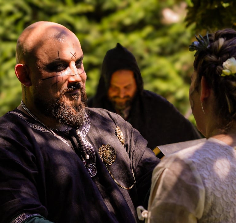 Hombre con maquillaje y tatuajes faciales vestido con traje medieval oscuro, mirando a su pareja dur