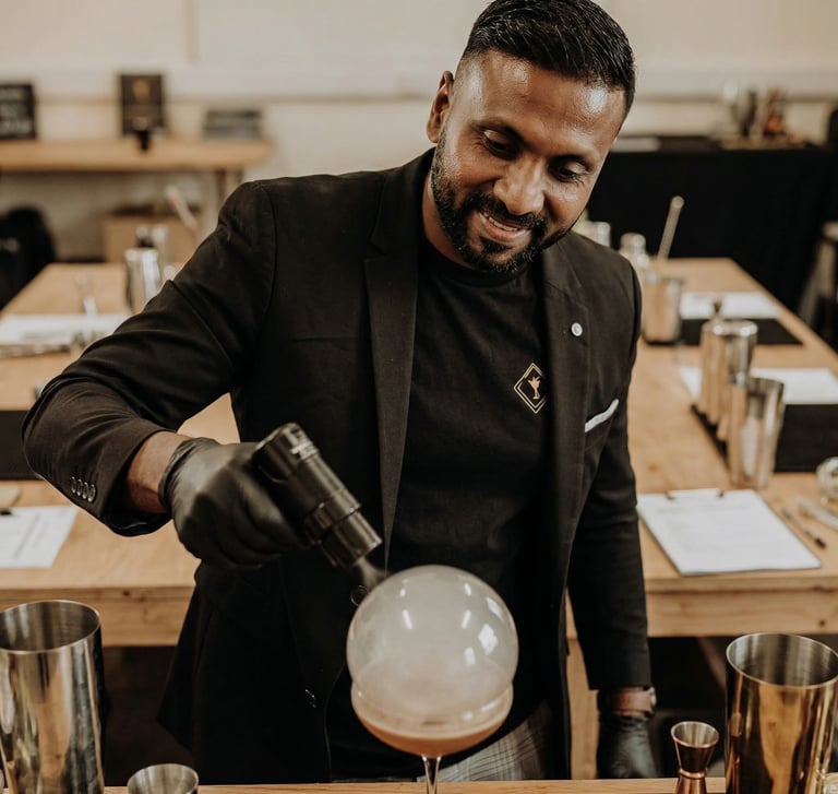 Professional mixologist using a torch to create a smoke bubble on a craft cocktail at a bar.