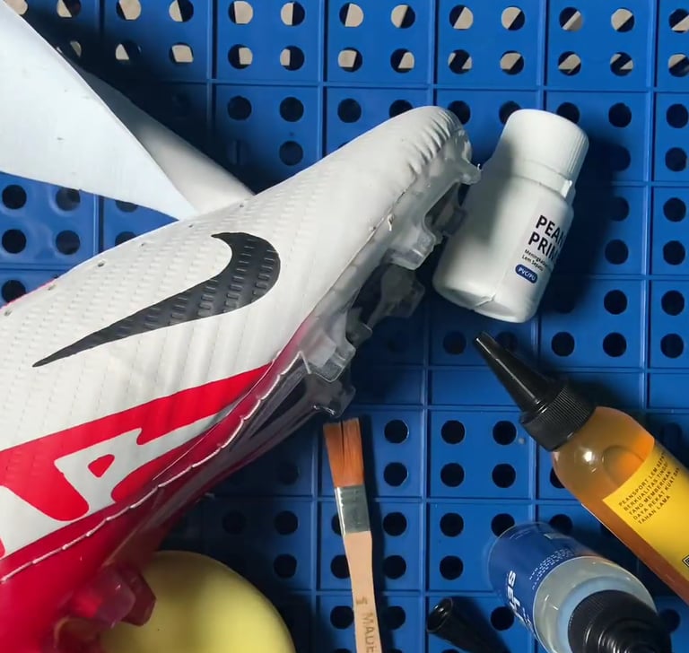 White and red Nike soccer cleat being repaired with shoe glue and brushes on a blue pegboard.