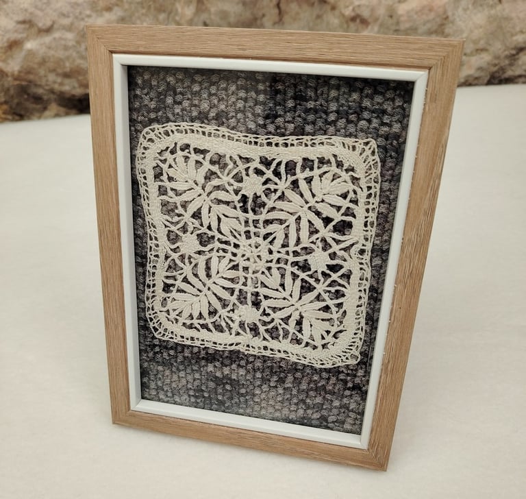 Ancien motif couleur crème fait au fuseau posé sur un fond tricoté en dégradé de gris