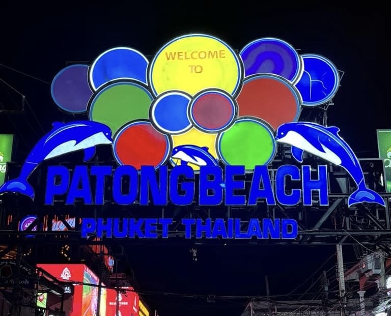 Beleuchtetes Neonschild von Patong Beach in Phuket, mit bunten Lichtern und Delfin-Figuren bei Nacht