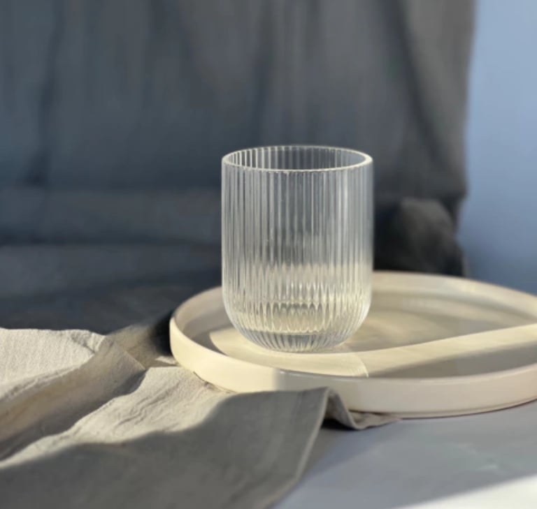 Elegant ribbed glass tumbler sitting on a white ceramic tray with soft linen textures.