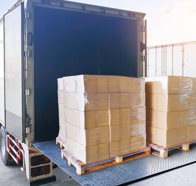 Stacked cardboard boxes on pallets being loaded into a delivery truck for shipping logistics.