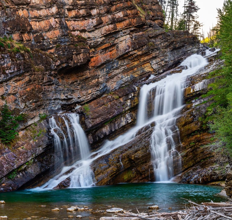 Cameron Falls cascading over layered red rock into a turquoise pool in Waterton Lakes National Park,