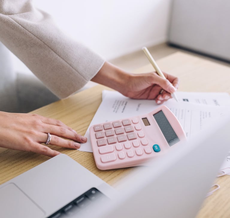 Businesswoman using a pink calculator and pen to calculate business finances and invoices at a desk.