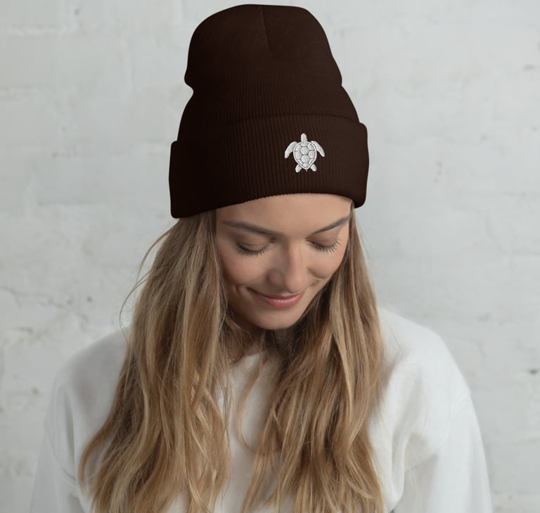A woman wearing a dark brown cuffed beanie with a white sea turtle embroidery.