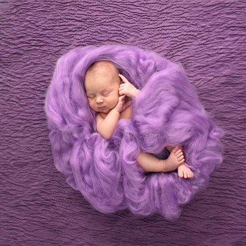 a newborn girl sleeping in a purple blanket
