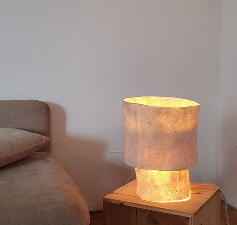 Handmade textile lamp glowing on a wooden side table next to a neutral couch.